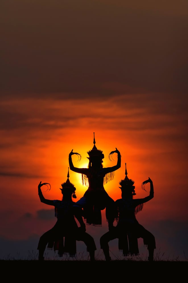 The black silhouette of three Manohra actors dancing in the park in the evening.